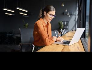 young adult working at desk in office with laptop