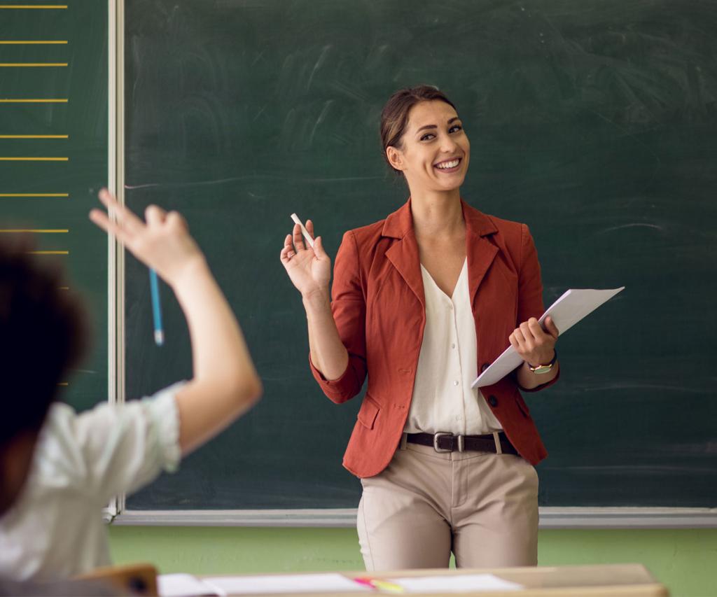 woman teacher standing in front of a blackboard answering questions from the class
